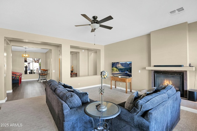 living room featuring ceiling fan with notable chandelier, wood-type flooring, and a tile fireplace