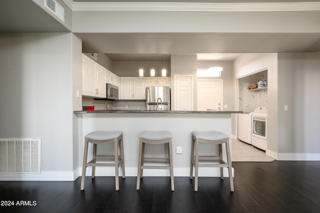 kitchen with a breakfast bar, white cabinets, appliances with stainless steel finishes, washer / dryer, and kitchen peninsula