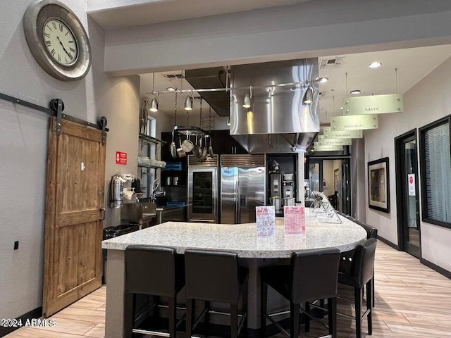 kitchen featuring a kitchen breakfast bar, a barn door, built in refrigerator, and light stone counters