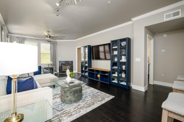 living room with a tile fireplace, dark hardwood / wood-style flooring, ceiling fan, and crown molding