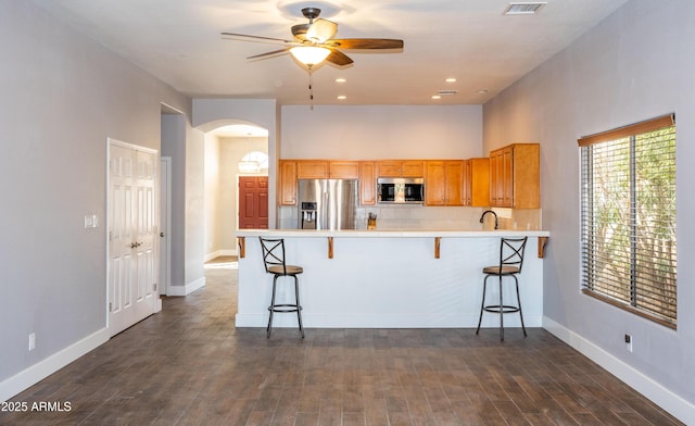 kitchen featuring stainless steel appliances, dark wood-type flooring, a kitchen breakfast bar, and kitchen peninsula