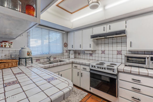 kitchen featuring decorative backsplash, stainless steel range with electric cooktop, white cabinetry, tile counters, and sink