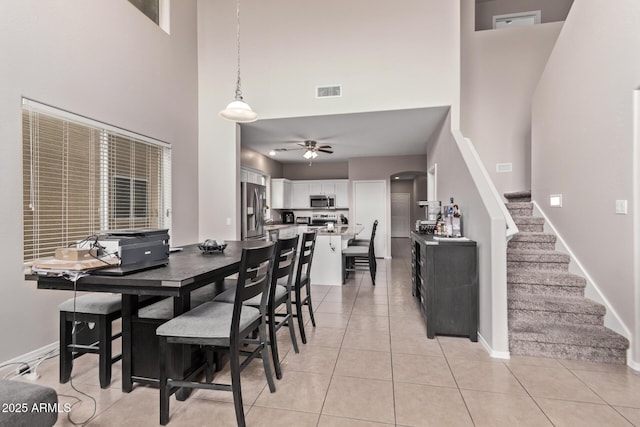 tiled dining space featuring ceiling fan and a high ceiling