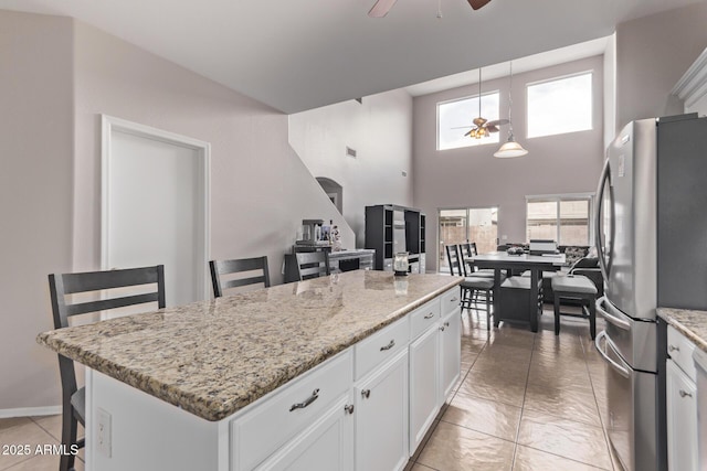 kitchen featuring white cabinetry, decorative light fixtures, stainless steel fridge, a kitchen island, and light stone countertops