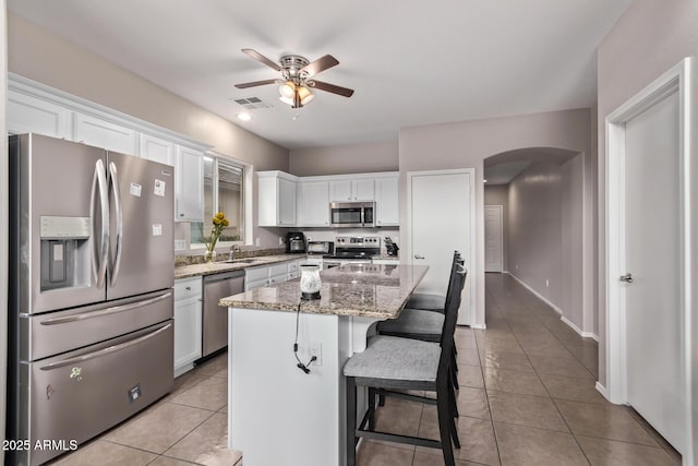 kitchen with a kitchen island, white cabinetry, appliances with stainless steel finishes, and light stone counters