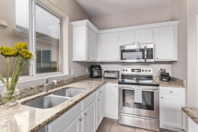 kitchen with sink, light tile patterned floors, appliances with stainless steel finishes, light stone countertops, and white cabinets