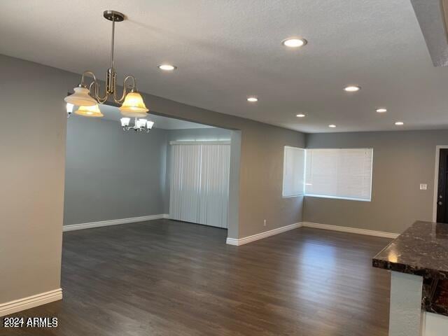 unfurnished living room with a textured ceiling, a chandelier, and dark hardwood / wood-style floors