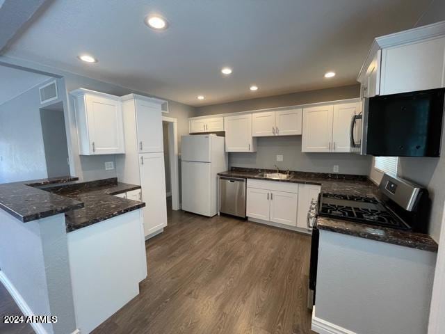 kitchen with dark hardwood / wood-style flooring, stainless steel appliances, sink, kitchen peninsula, and dark stone countertops