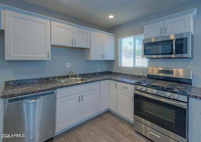 kitchen featuring light wood-type flooring, dark stone counters, white cabinetry, sink, and appliances with stainless steel finishes