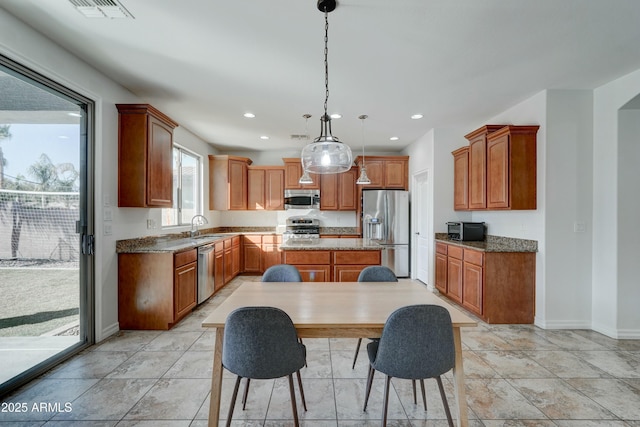 kitchen featuring light stone counters, appliances with stainless steel finishes, decorative light fixtures, and a center island