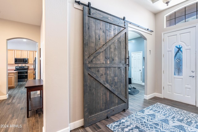 foyer featuring arched walkways, baseboards, a barn door, and dark wood-style flooring