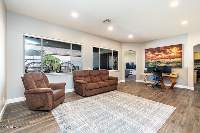 living room with arched walkways, visible vents, baseboards, and wood finished floors