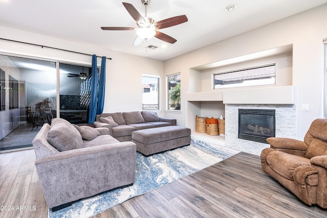 living area featuring visible vents, ceiling fan, a glass covered fireplace, and wood finished floors