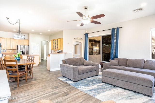 living area with light wood-type flooring, visible vents, recessed lighting, arched walkways, and ceiling fan