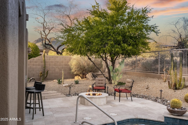 patio terrace at dusk featuring a fenced backyard and an outdoor fire pit