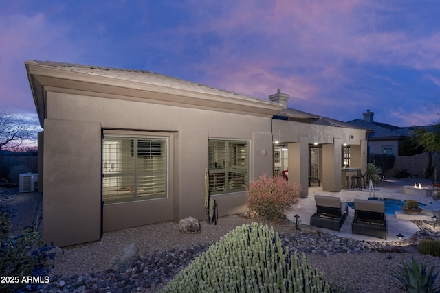 rear view of property featuring an outdoor fire pit, stucco siding, a patio, and central AC