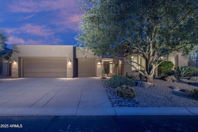 pueblo revival-style home featuring a garage, concrete driveway, and stucco siding