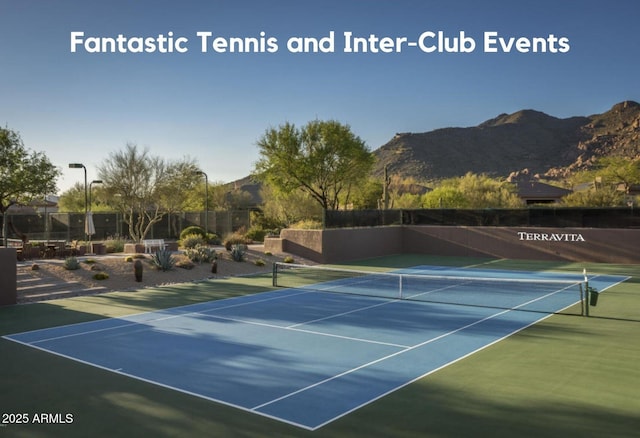 view of tennis court with a mountain view and fence