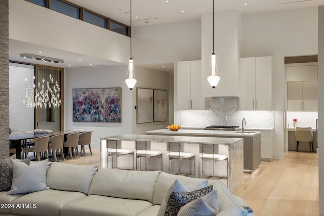 kitchen with a towering ceiling, a kitchen island with sink, pendant lighting, light hardwood / wood-style flooring, and white cabinets