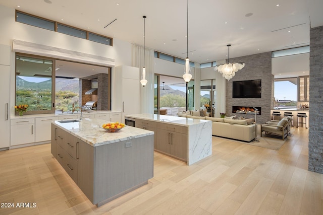 kitchen featuring sink, an island with sink, pendant lighting, and wall chimney range hood