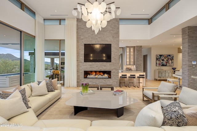 living room featuring a mountain view, a high ceiling, a stone fireplace, light wood-type flooring, and a notable chandelier