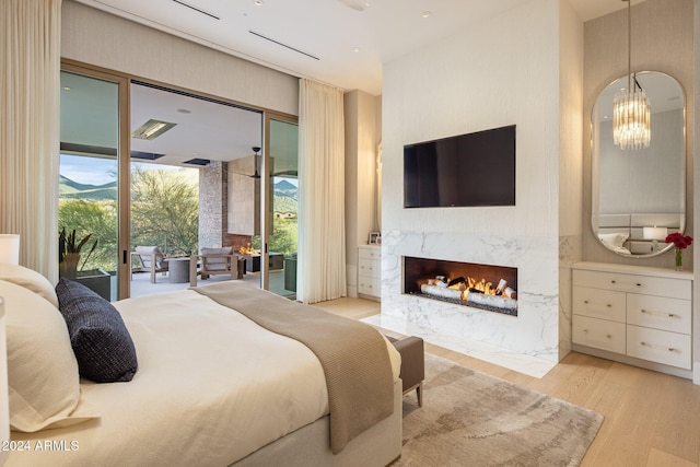 bedroom with access to exterior, a fireplace, a notable chandelier, and light hardwood / wood-style flooring