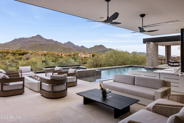 view of patio featuring a mountain view, ceiling fan, and an outdoor living space with a fire pit