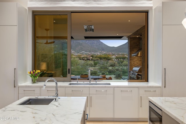 kitchen with white cabinets, a mountain view, light stone counters, and sink