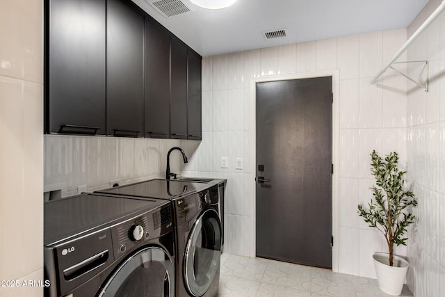 washroom with visible vents, washer and clothes dryer, cabinet space, and tile walls