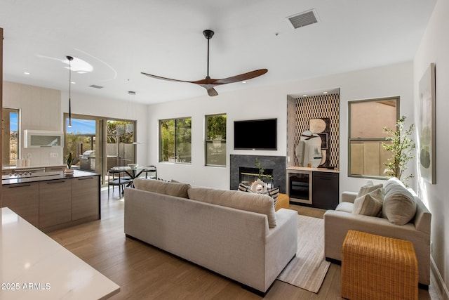 living area featuring light wood finished floors, a fireplace, visible vents, and a ceiling fan