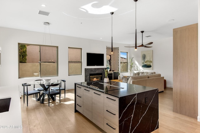 kitchen with light wood-style flooring, a glass covered fireplace, visible vents, dark countertops, and modern cabinets