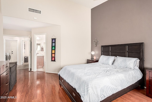 bedroom featuring separate washer and dryer, wood finished floors, visible vents, baseboards, and ensuite bath