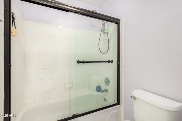 bathroom featuring toilet and shower / bath combination with glass door