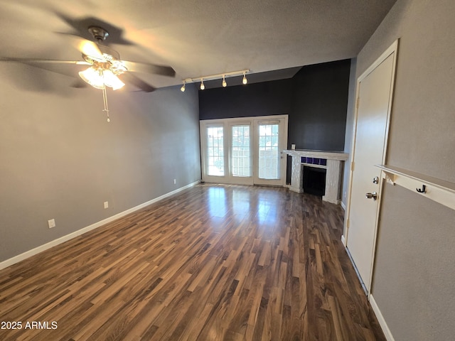 unfurnished living room with dark wood-type flooring, rail lighting, a fireplace, baseboards, and ceiling fan