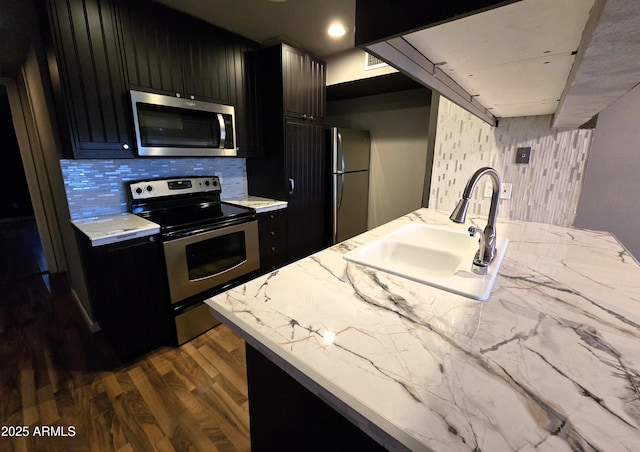 kitchen featuring a sink, backsplash, dark wood-style floors, stainless steel appliances, and dark cabinets