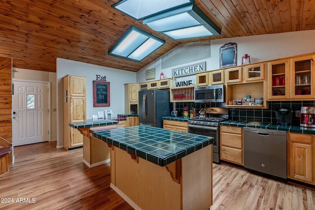 kitchen featuring vaulted ceiling with skylight, stainless steel appliances, a center island, tile countertops, and a breakfast bar area