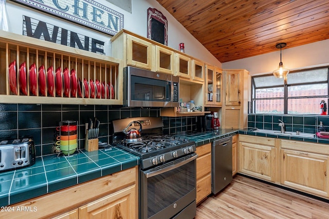 kitchen featuring pendant lighting, stainless steel appliances, vaulted ceiling, backsplash, and tile countertops