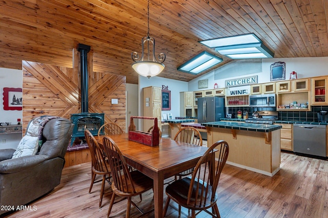 dining area with wood walls, a wood stove, vaulted ceiling, and light wood-type flooring