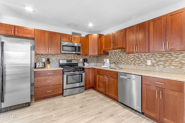 kitchen with light stone countertops, decorative backsplash, stainless steel appliances, sink, and light hardwood / wood-style floors