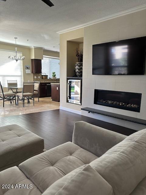 living room featuring a textured ceiling, a large fireplace, beverage cooler, hardwood / wood-style flooring, and a chandelier