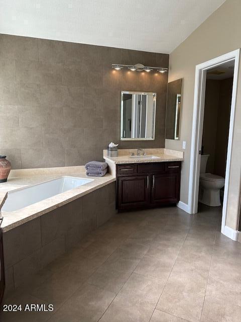 bathroom with tile patterned floors, vanity, a relaxing tiled tub, and toilet