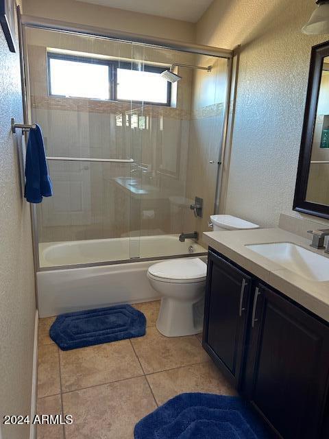 full bathroom with combined bath / shower with glass door, vanity, tile patterned flooring, and toilet