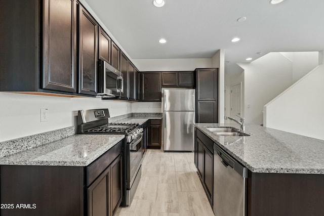 kitchen with sink, dark brown cabinets, stainless steel appliances, light stone countertops, and light wood-type flooring