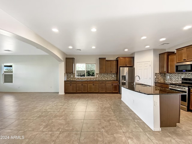 kitchen with decorative backsplash, sink, stainless steel appliances, and an island with sink