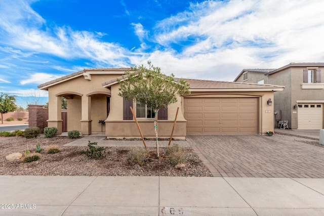 mediterranean / spanish-style house featuring a tiled roof, decorative driveway, an attached garage, and stucco siding