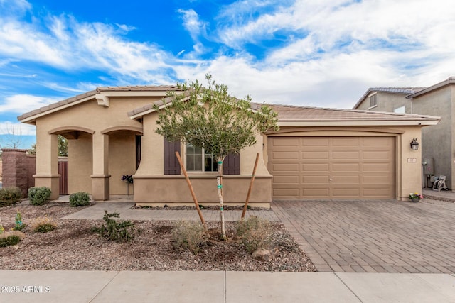 view of front facade featuring a tiled roof, decorative driveway, an attached garage, and stucco siding