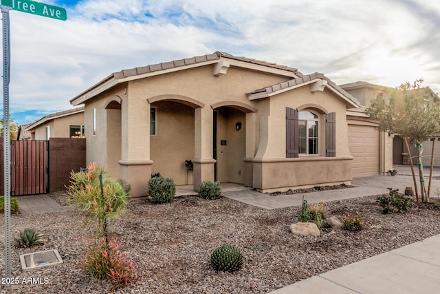 mediterranean / spanish-style home featuring stucco siding, concrete driveway, a gate, fence, and a garage