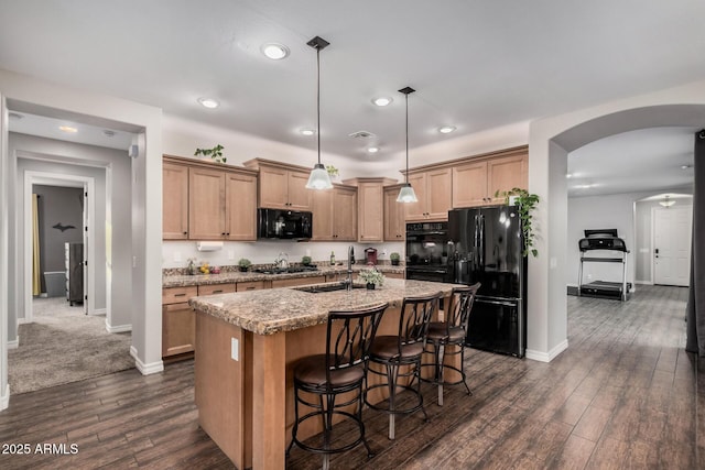 kitchen featuring dark wood-style floors, arched walkways, a breakfast bar area, an island with sink, and black appliances