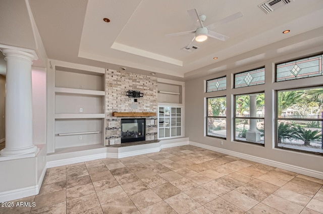 unfurnished living room with ornate columns, built in features, a large fireplace, ceiling fan, and a raised ceiling