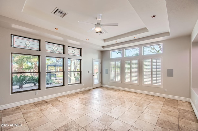 tiled empty room featuring a raised ceiling, a healthy amount of sunlight, and ceiling fan